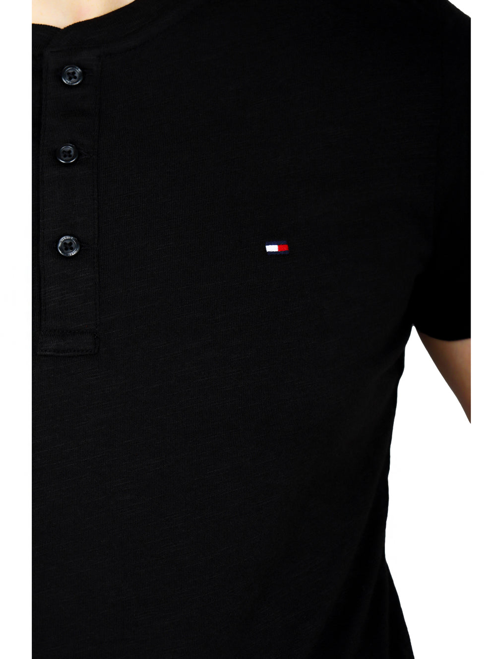 Hombre vistiendo una camiseta negra de manga corta con cuello henley y botones frontales de la marca Tommy Hilfiger.