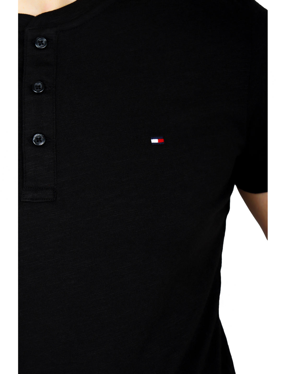 Hombre vistiendo una camiseta negra de manga corta con cuello henley y botones frontales de la marca Tommy Hilfiger.
