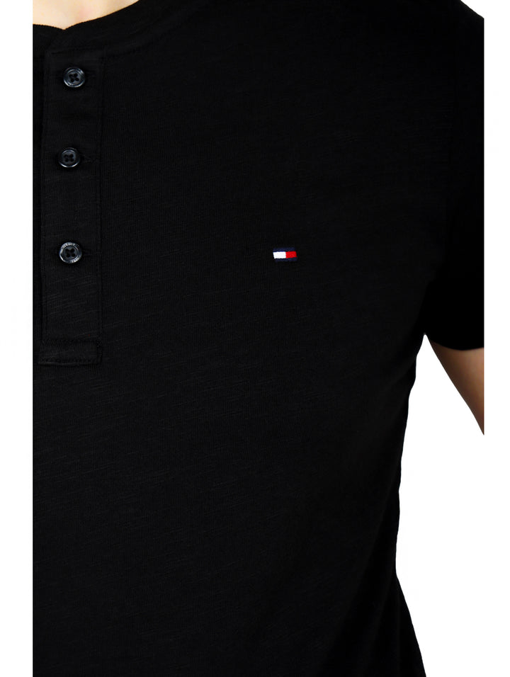 Hombre vistiendo una camiseta negra de manga corta con cuello henley y botones frontales de la marca Tommy Hilfiger.