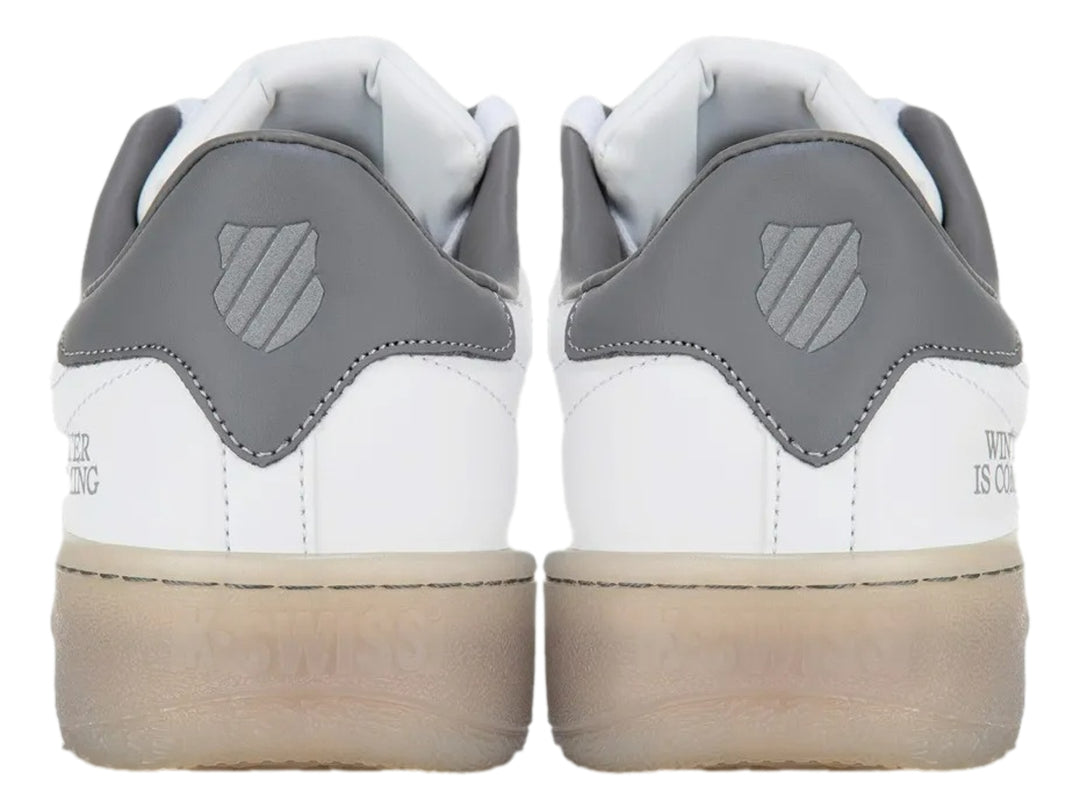Tenis K-Swiss blancos con detalle gris en el talón y suela translúcida beige.