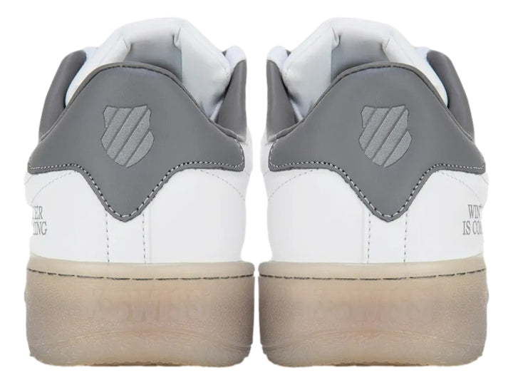 Tenis K-Swiss blancos con detalle gris en el talón y suela translúcida beige.