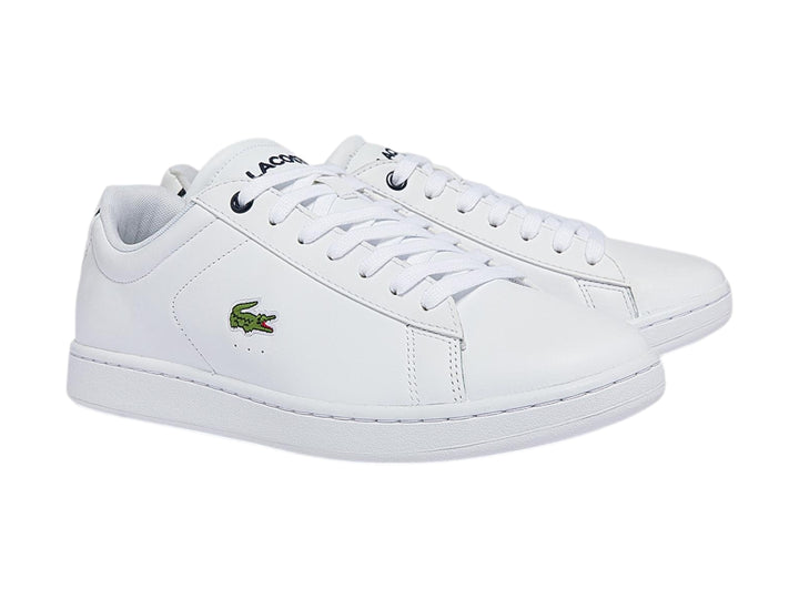 Tenis blancos de cuero marca Lacoste con logotipo del cocodrilo verde y detalle azul marino en el talón.