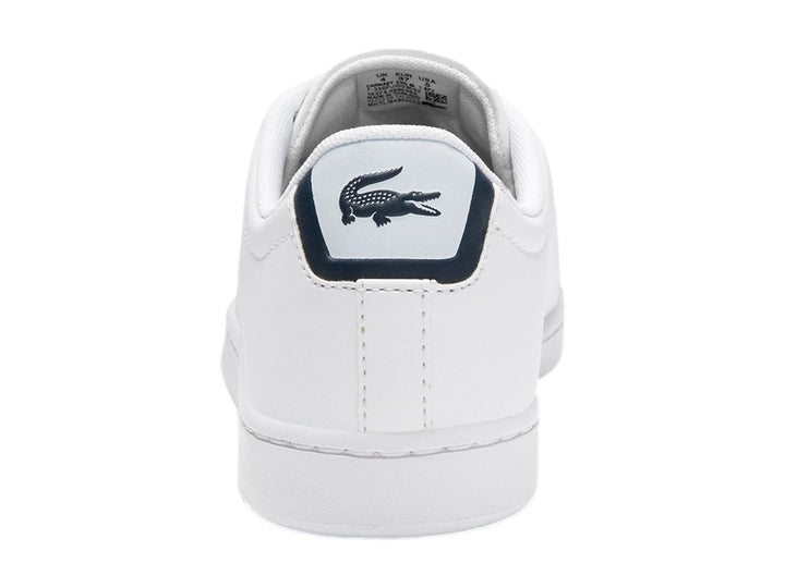 Tenis Lacoste blancos para niño con detalles en azul marino y logotipo de cocodrilo verde en el lateral.