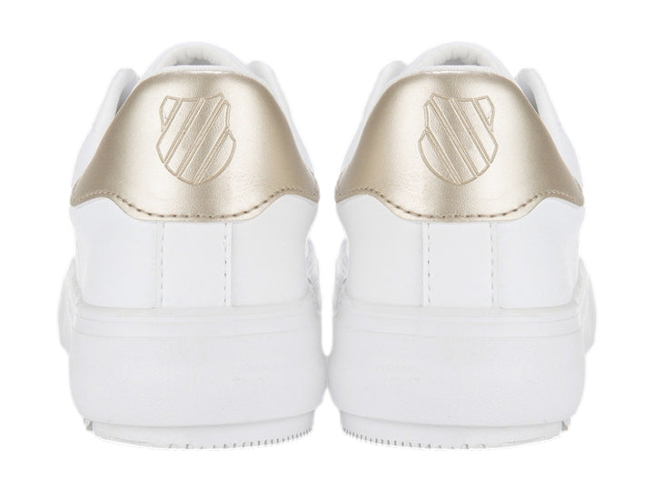 Tenis blancos K-Swiss con detalle dorado en el talón y cordones blancos.