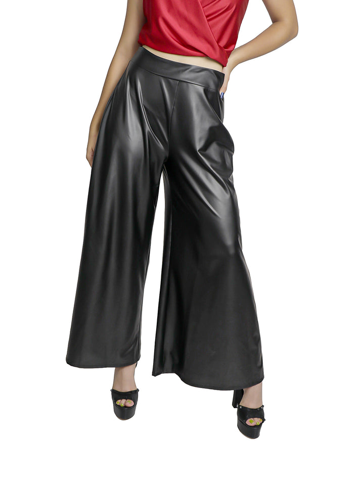 Mujer vistiendo pantalón negro de piel sintética con corte ancho y acabado brillante.