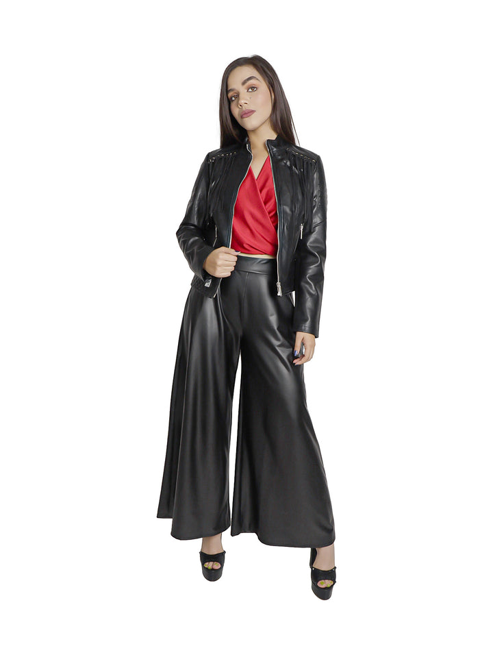 Mujer vistiendo pantalón negro de piel sintética con corte ancho y acabado brillante.