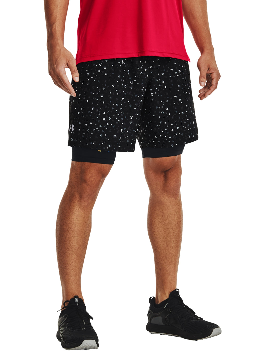 Hombre vistiendo shorts deportivos Under Armour color negro con estampado de pequeños puntos blancos.