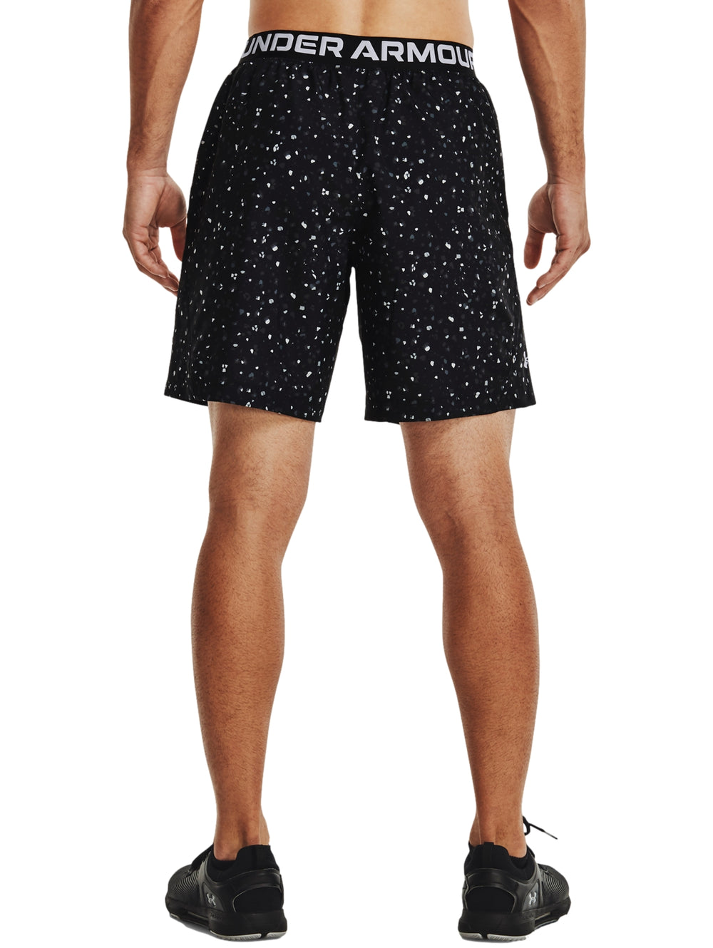 Hombre vistiendo shorts deportivos Under Armour color negro con estampado de pequeños puntos blancos.