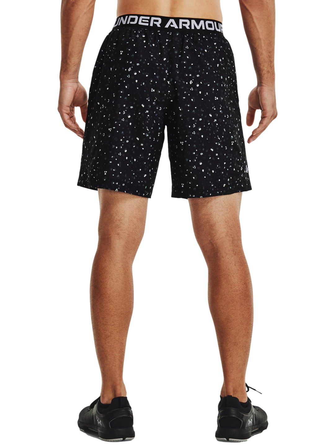 Hombre vistiendo shorts deportivos Under Armour color negro con estampado de pequeños puntos blancos.