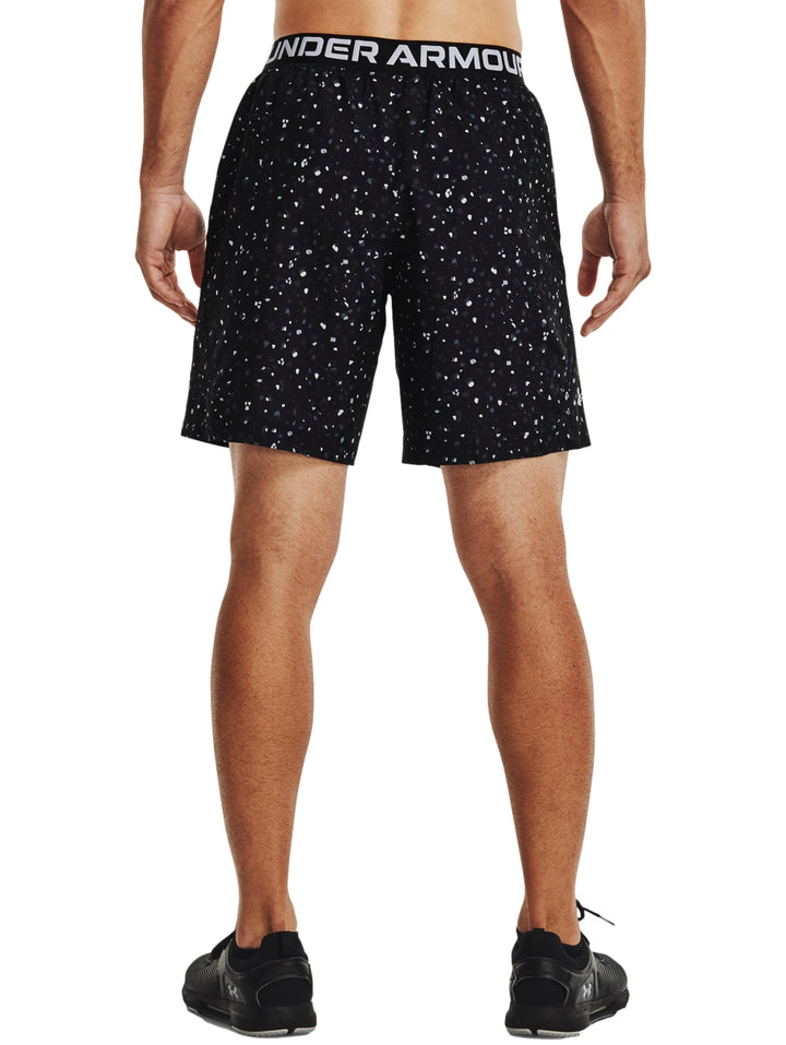 Hombre vistiendo shorts deportivos Under Armour color negro con estampado de pequeños puntos blancos.