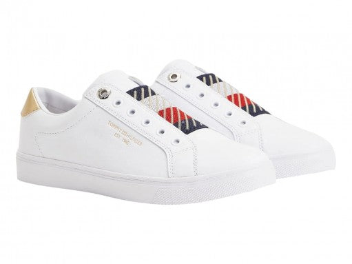 Tenis blancos Tommy Hilfiger estilo slip-on con detalle dorado en el talón y suela blanca.
