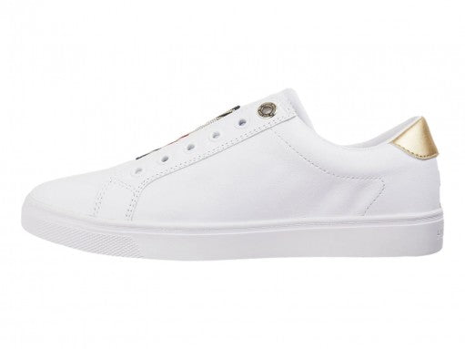 Tenis blancos Tommy Hilfiger estilo slip-on con detalle dorado en el talón y suela blanca.