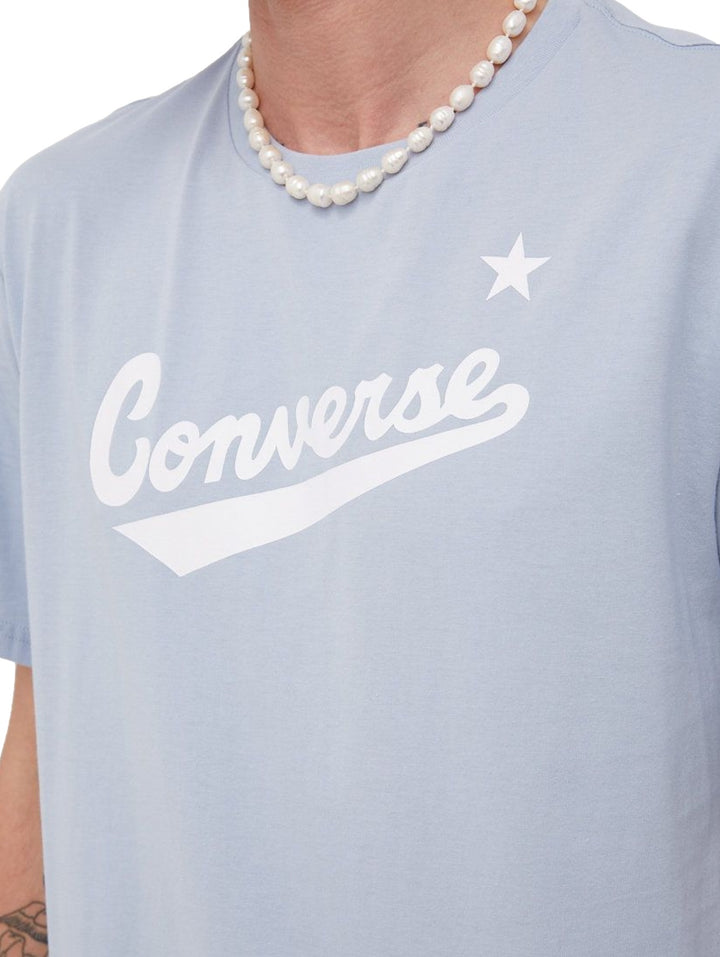 Hombre usando una playera Converse de color azul claro con logotipo blanco en el pecho.