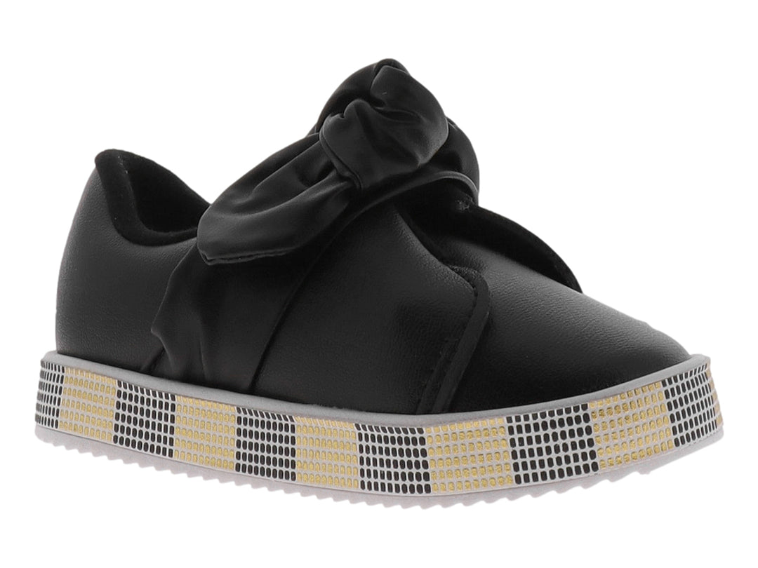 Zapato negro para niña con moño decorativo y suela con patrón de cuadros negros y dorados.