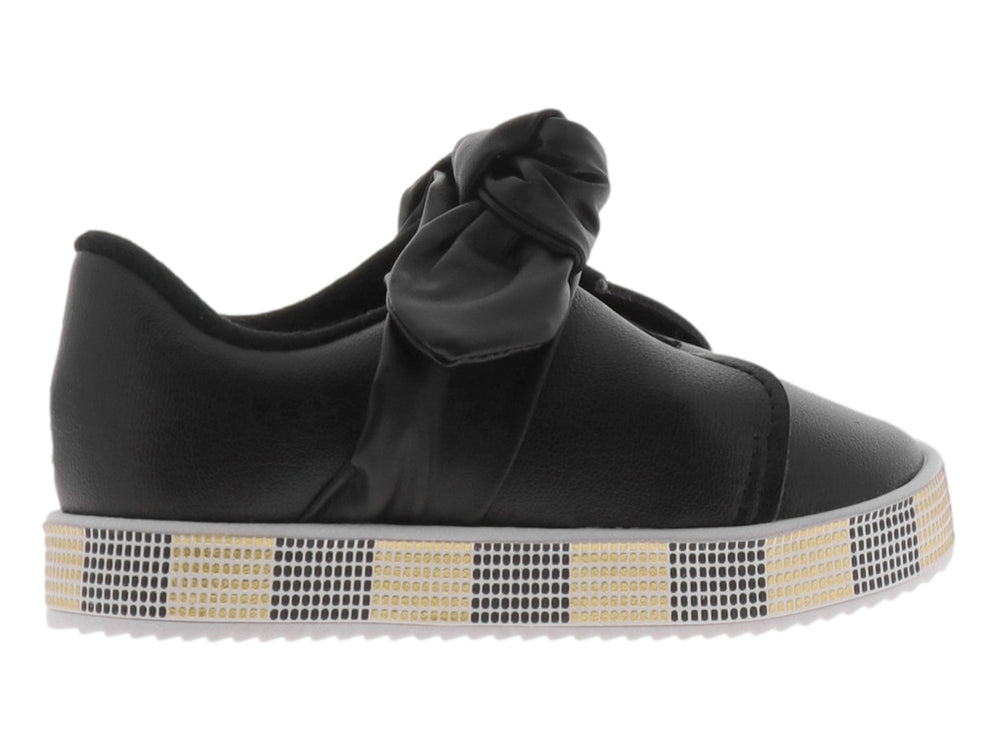 Zapato negro para niña con moño decorativo y suela con patrón de cuadros negros y dorados.