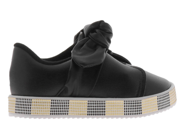 Zapato negro para niña con moño decorativo y suela con patrón de cuadros negros y dorados.