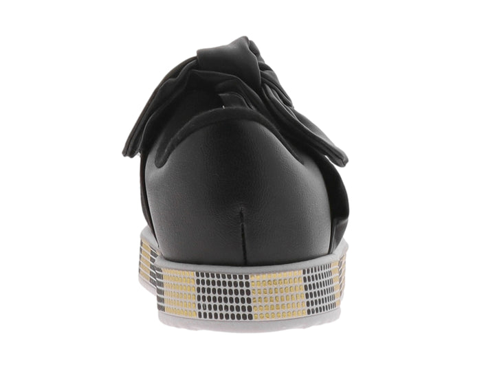 Zapato negro para niña con moño decorativo y suela con patrón de cuadros negros y dorados.