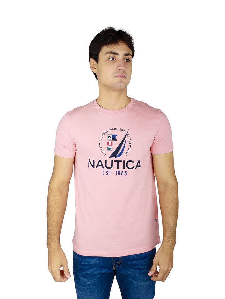 Hombre vistiendo playera Nautica de color rosa con logotipo estampado en el pecho y pantalones mezclilla azules.