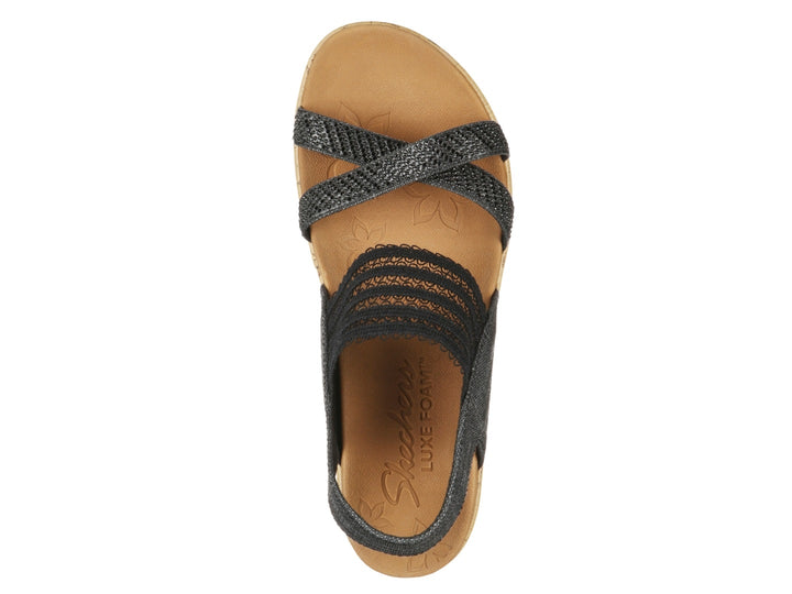 Sandalia de cuña Skechers con tiras negras de tela y plataforma de corcho color beige.