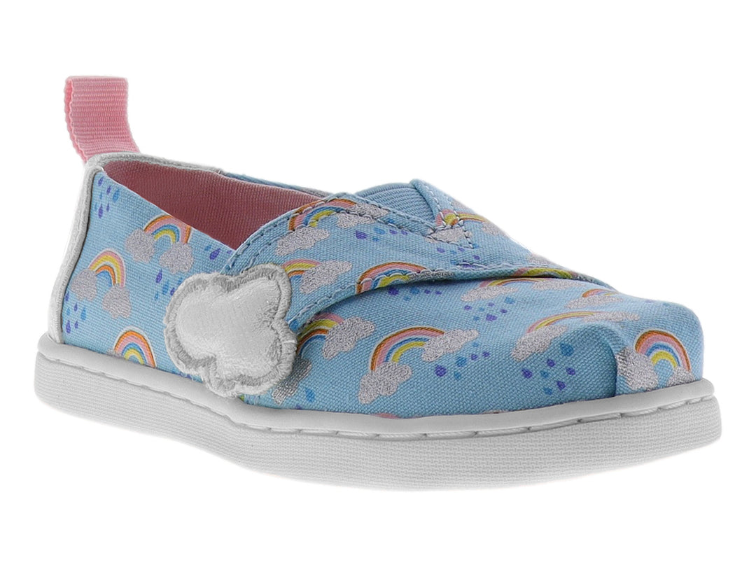 Zapato slip-on azul para niña con estampado de arcoíris, detalle de nube blanca y talón rosa.