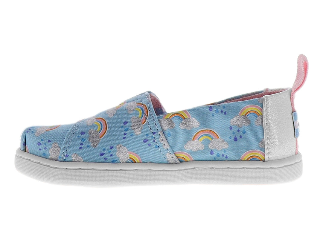 Zapato slip-on azul para niña con estampado de arcoíris, detalle de nube blanca y talón rosa.