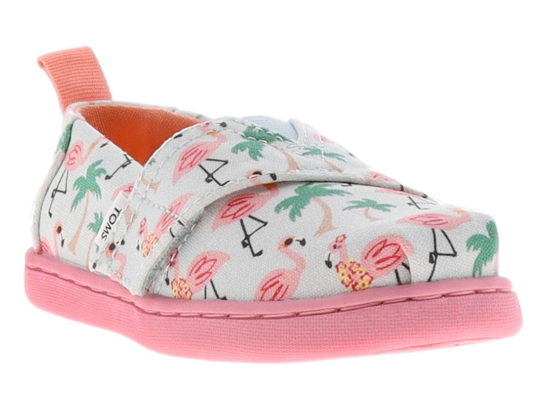 Zapato TOMS infantil azul claro con estampado de flamencos rosas y palmeras, con suela rosa.