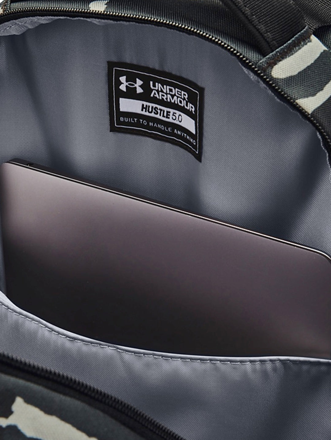 Mochila Under Armour Hustle 5.0 con estampado de camuflaje en tonos negro y gris con logos dorados.