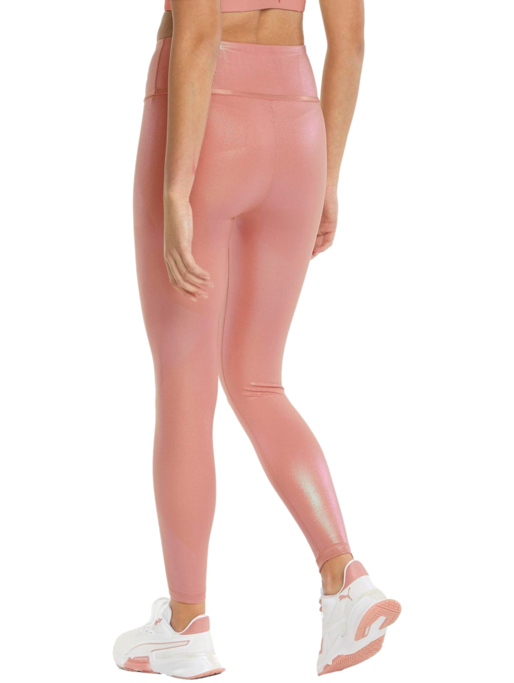 Mujer vistiendo leggings PUMA de color rosa iridiscente con talle alto y tenis blancos.