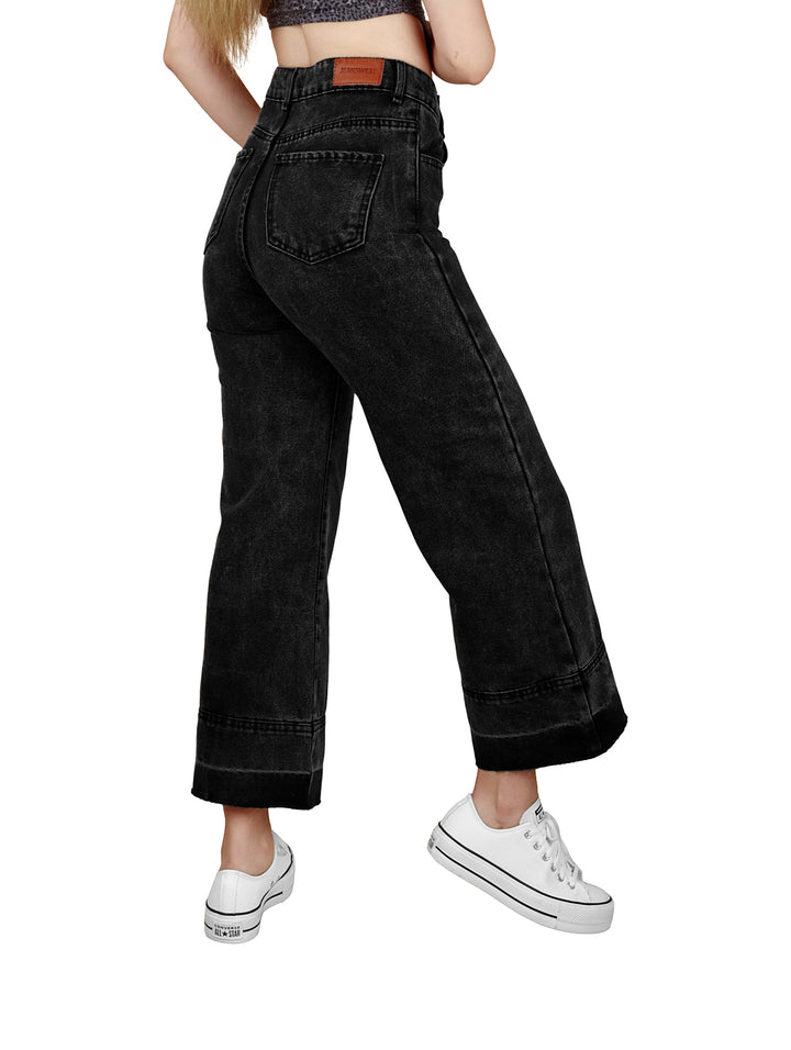 Mujer vistiendo jeans negros de corte pata elefante y tenis blancos sobre fondo blanco.