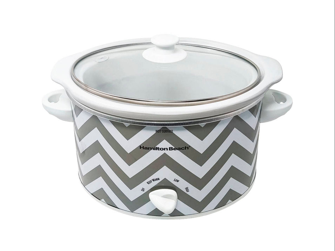 Olla de cocción lenta Hamilton Beach blanca con diseño de zig-zag gris y tapa de vidrio transparente.