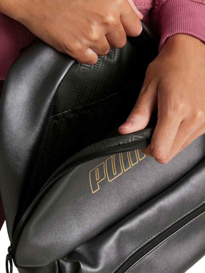 Mochila Puma color negro con logotipo metálico dorado en el centro y bolsillo frontal con cierre.