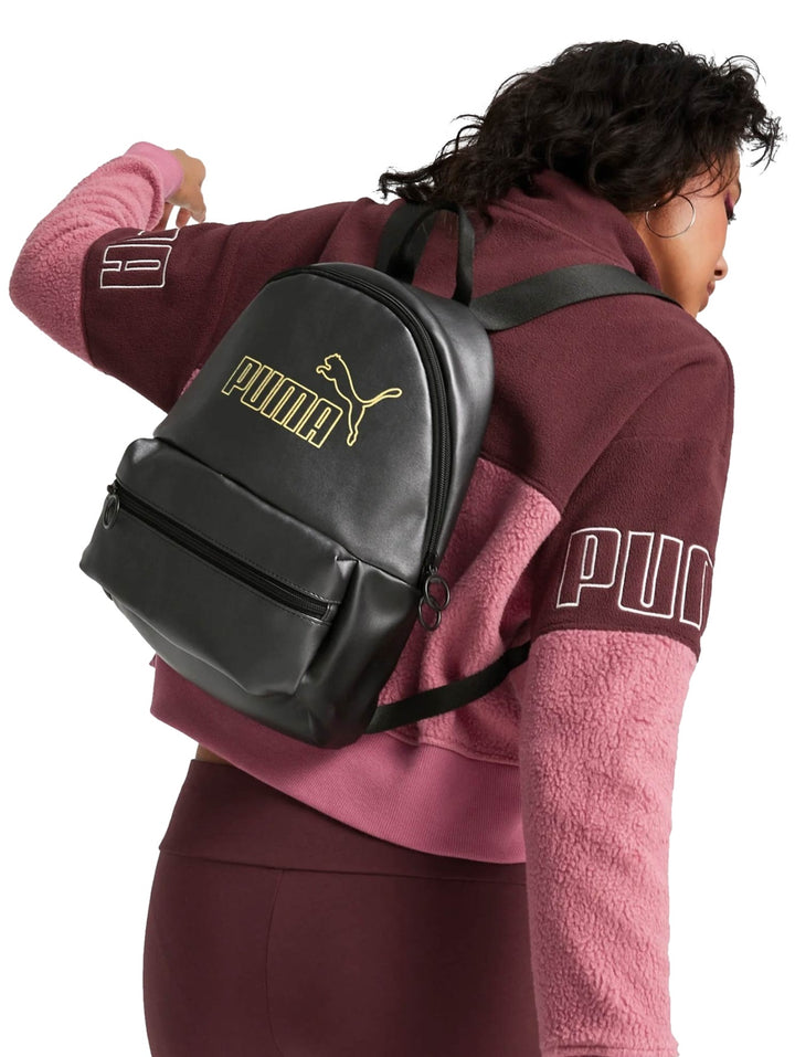 Mochila Puma color negro con logotipo metálico dorado en el centro y bolsillo frontal con cierre.
