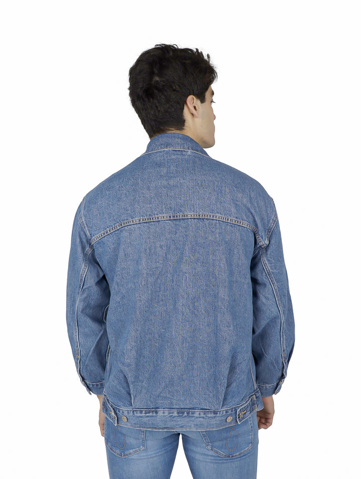 Hombre vistiendo una chaqueta de mezclilla azul claro de corte holgado y pantalones a juego.