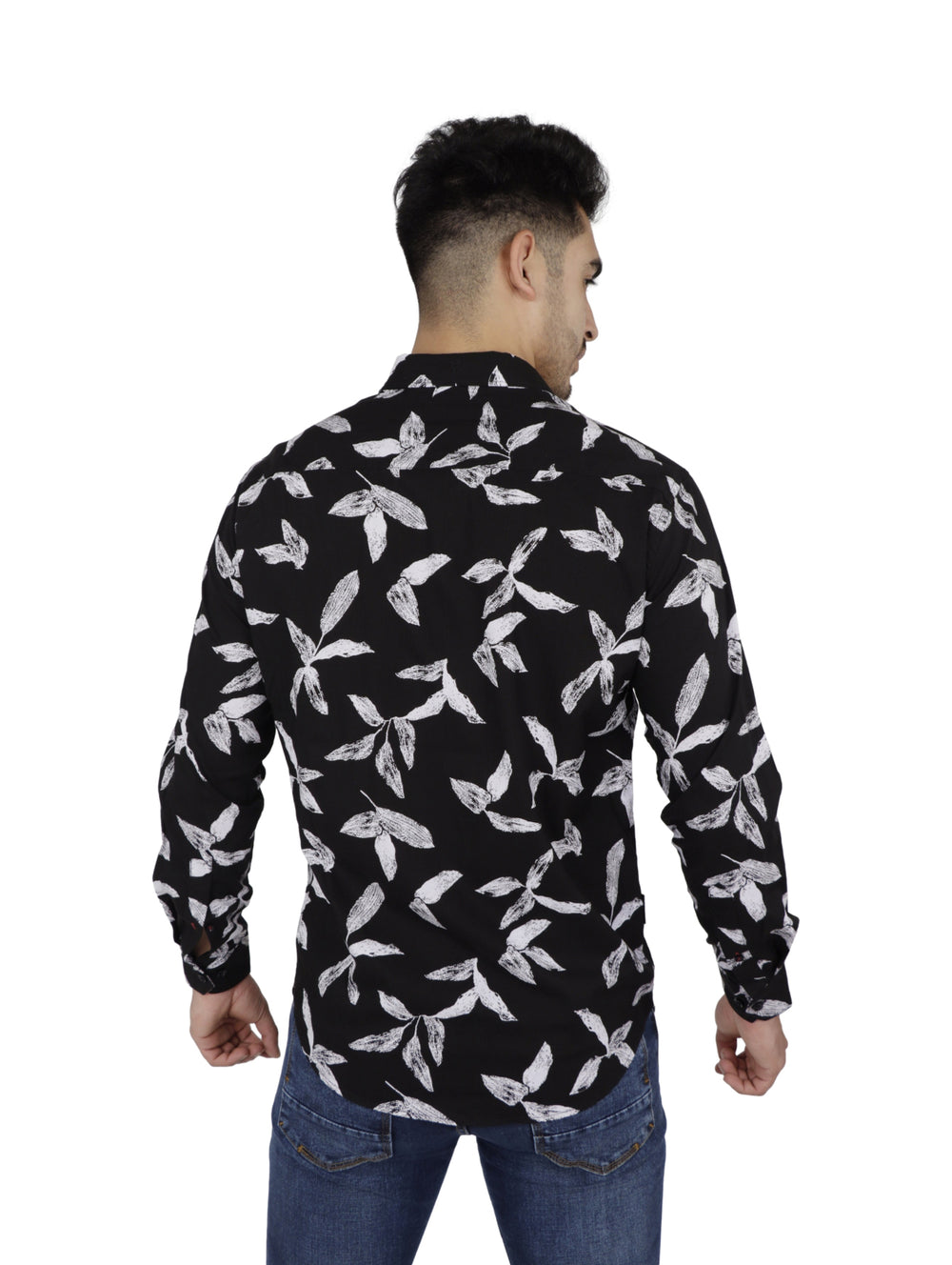 Hombre vistiendo camisa negra de manga larga con estampado de hojas blancas y pantalones vaqueros azules.