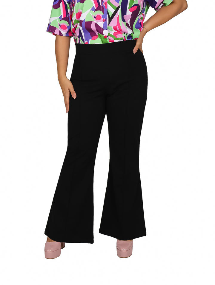 Mujer usando pantalón negro acampanado de talle alto con blusa multicolor y zapatos rosas.