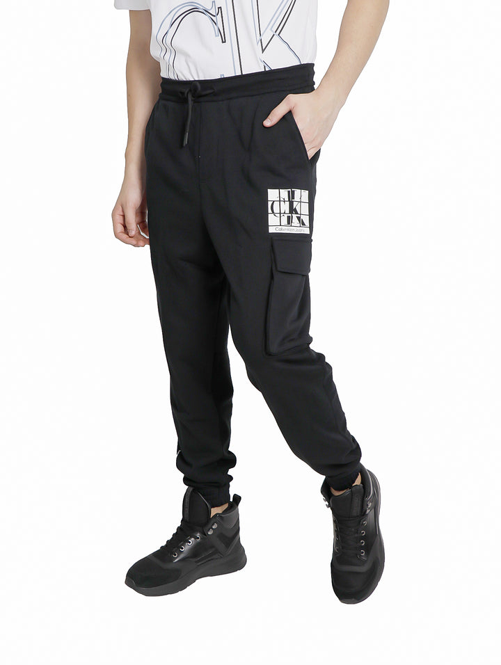 Hombre vistiendo pantalones urbanos negros de Calvin Klein con gráfico CK y bolsillo cargo.