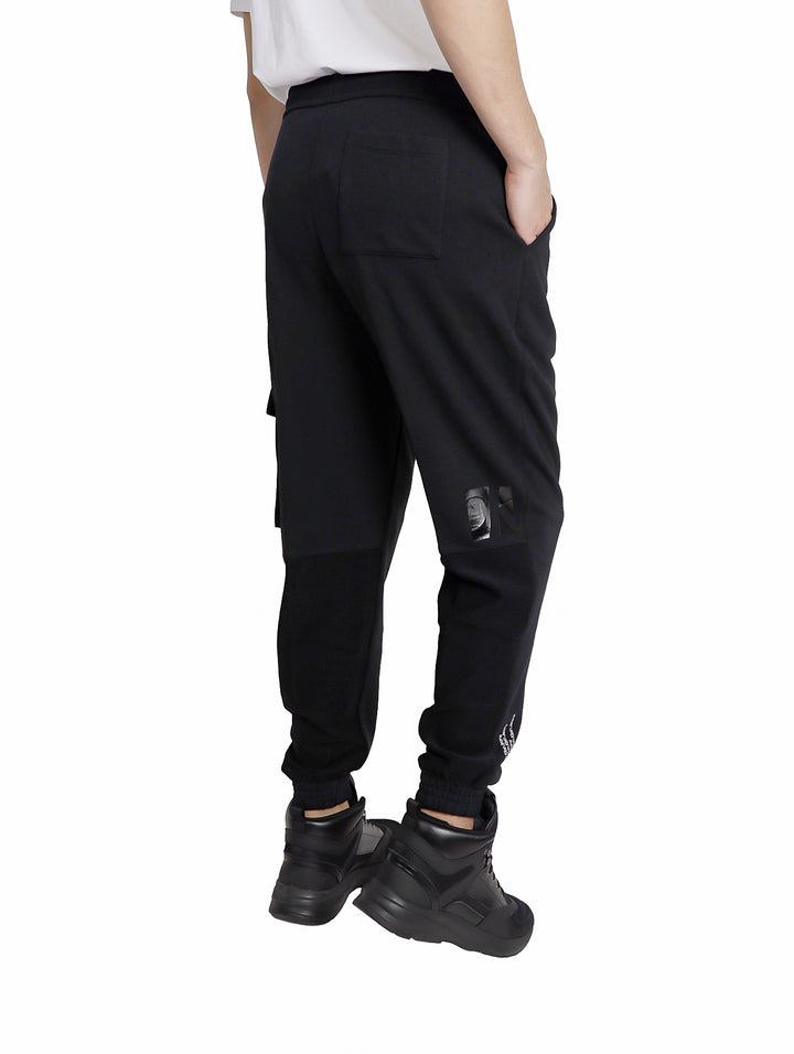 Hombre vistiendo pantalones urbanos negros de Calvin Klein con gráfico CK y bolsillo cargo.