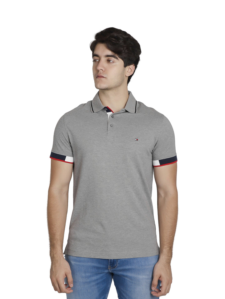 Hombre vistiendo polo Tommy Hilfiger color gris jaspeado con detalles tricolores en los puños y cuello.