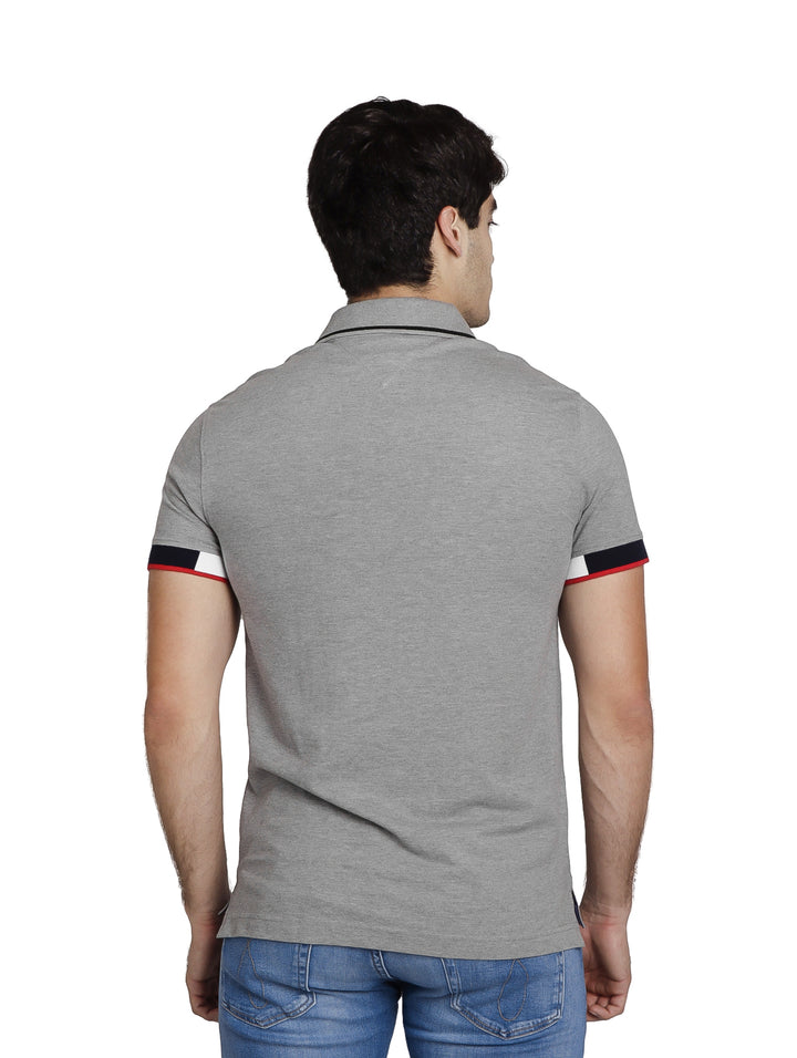Hombre vistiendo polo Tommy Hilfiger color gris jaspeado con detalles tricolores en los puños y cuello.