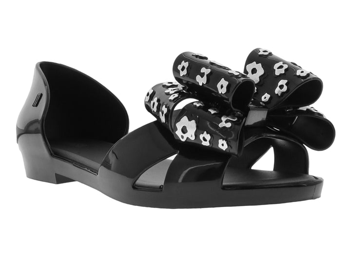Zapato plano negro con moño decorativo con estampado de flores blancas.