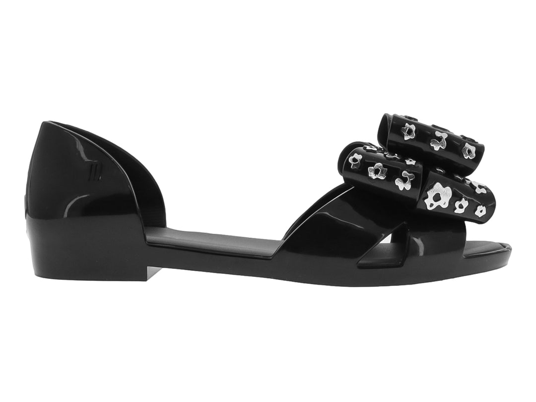 Zapato plano negro con moño decorativo con estampado de flores blancas.