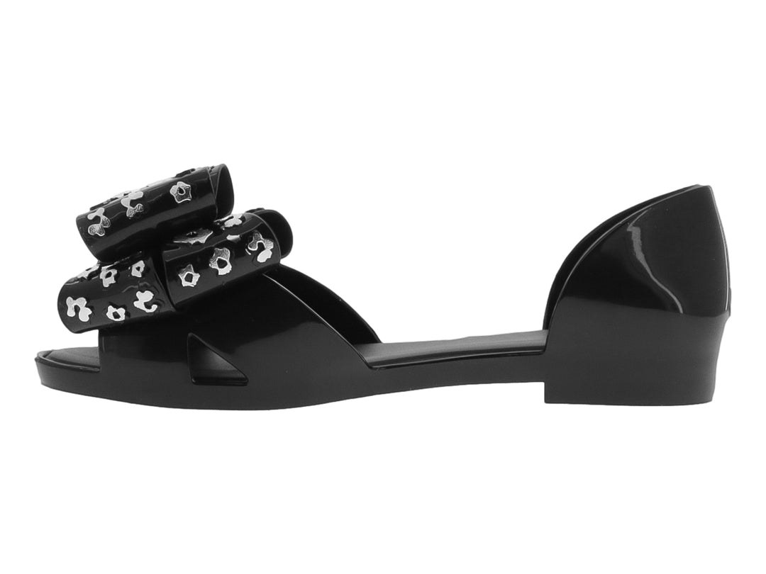 Zapato plano negro con moño decorativo con estampado de flores blancas.