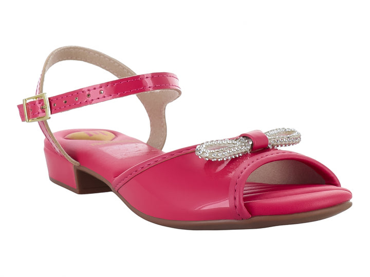 Sandalia rosa brillante para niña con moño decorativo y correa al tobillo.