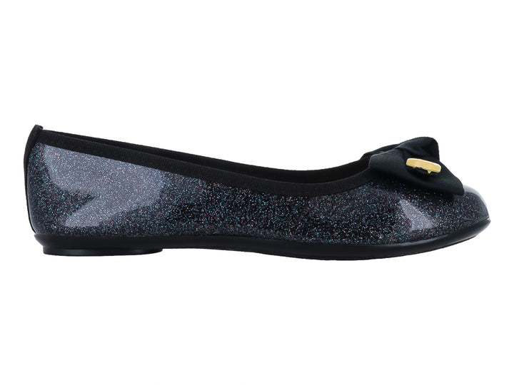 Zapato plano negro con acabado brillante y glitter, decorado con un moño negro y pequeños corazones amarillos y rosas.