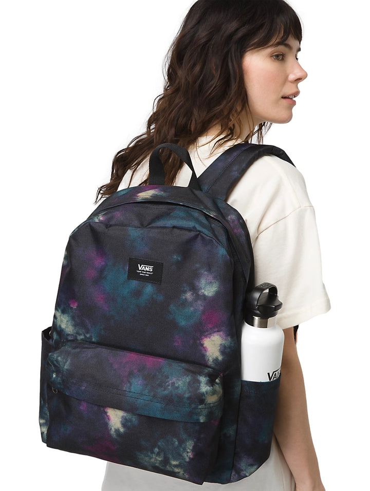 Mochila Vans con estampado multicolor estilo tie-dye en tonos negro, morado y azul, portada por una mujer.