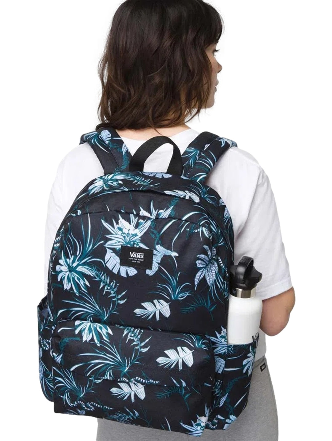 Mochila Vans color negro con estampado de hojas tropicales en blanco y azul, portada por una mujer.