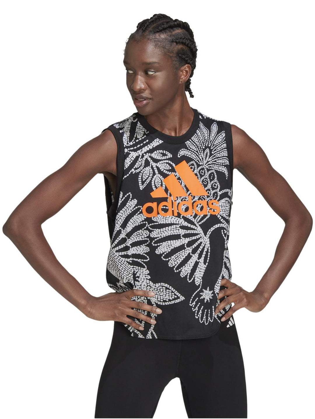 Mujer vistiendo una camiseta sin mangas Adidas negra con estampado floral blanco y logotipo naranja frontal.