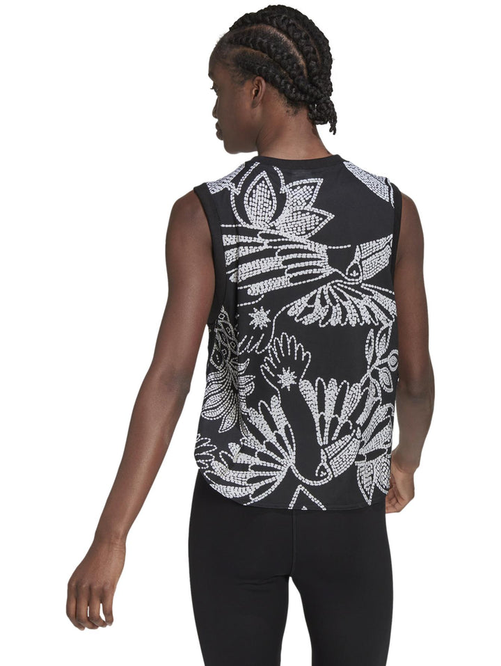 Mujer vistiendo una camiseta sin mangas Adidas negra con estampado floral blanco y logotipo naranja frontal.