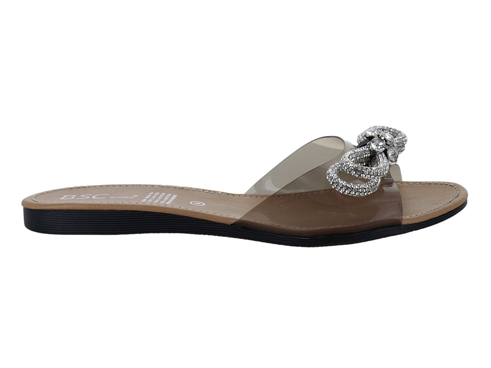 Sandalia plana con tira transparente, moño de pedrería brillante, plantilla beige y suela negra.