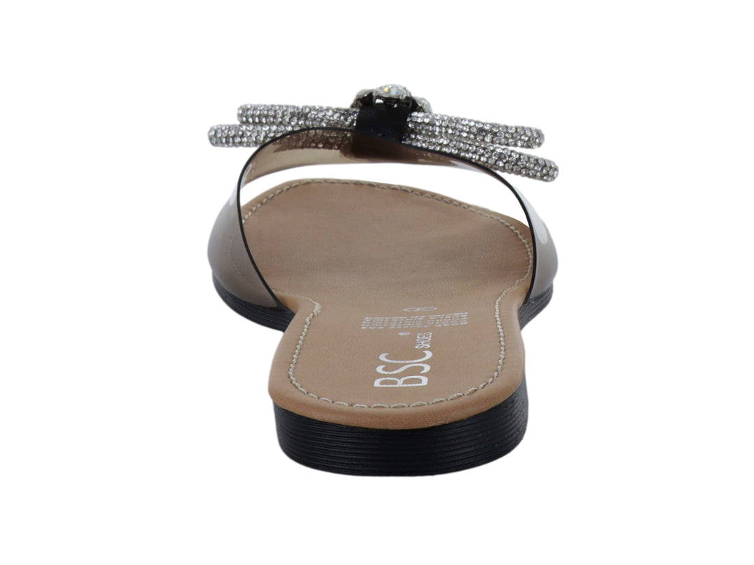 Sandalia plana con tira transparente, moño de pedrería brillante, plantilla beige y suela negra.